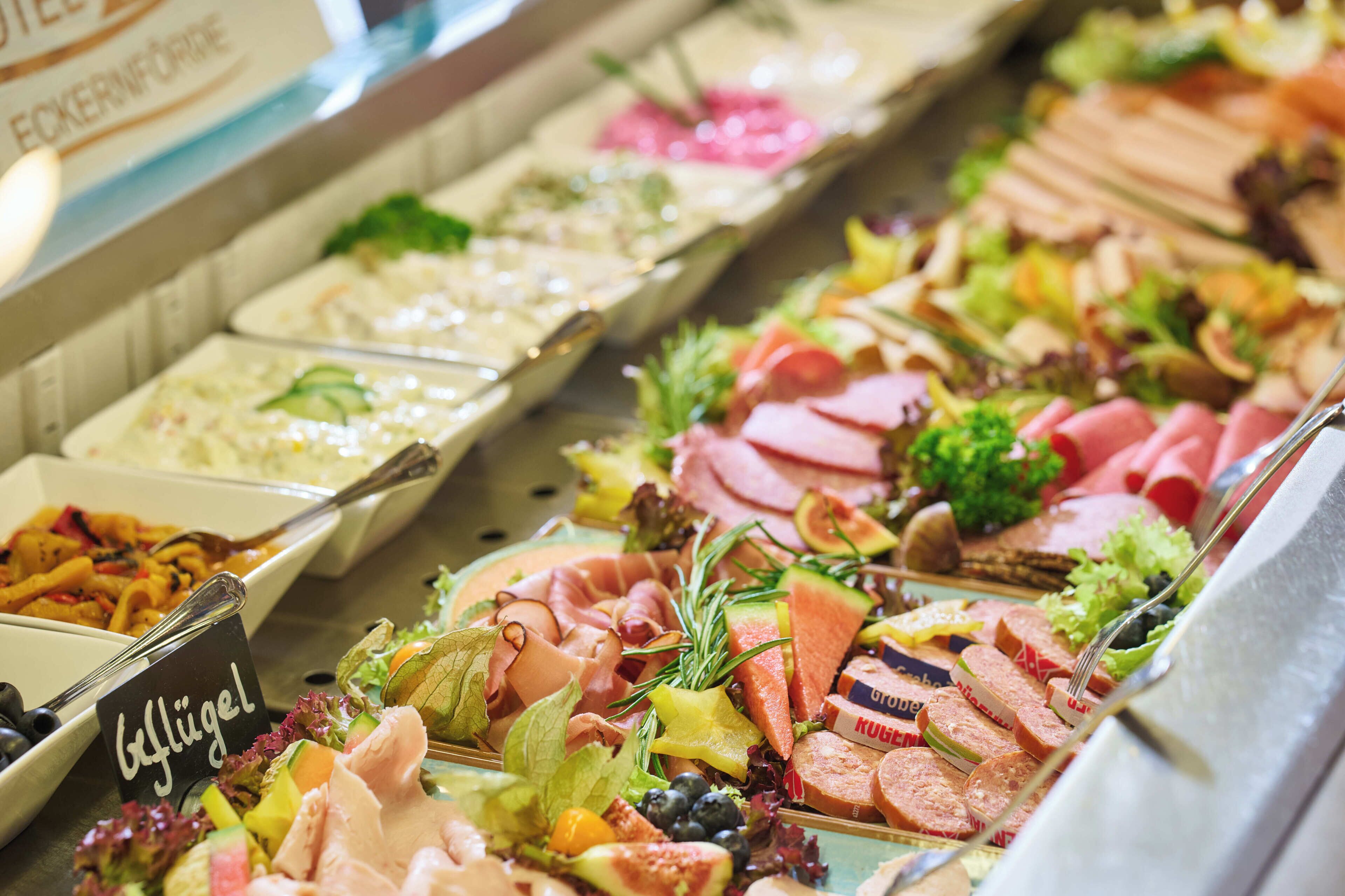 Ein reichhaltiges Buffet mit verschiedenen Speisen, darunter Fleisch, Salate und Obst.