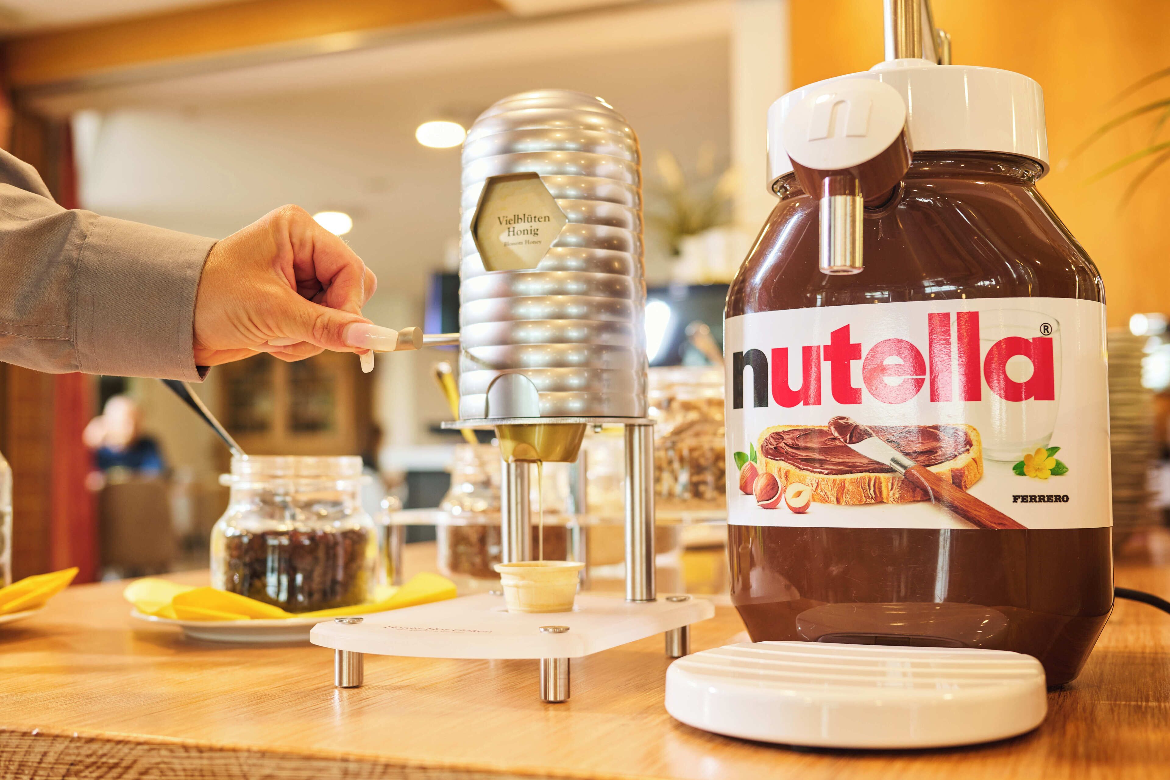 A Nutella dispenser with a jar of Nutella and a hand holding a spoon.
