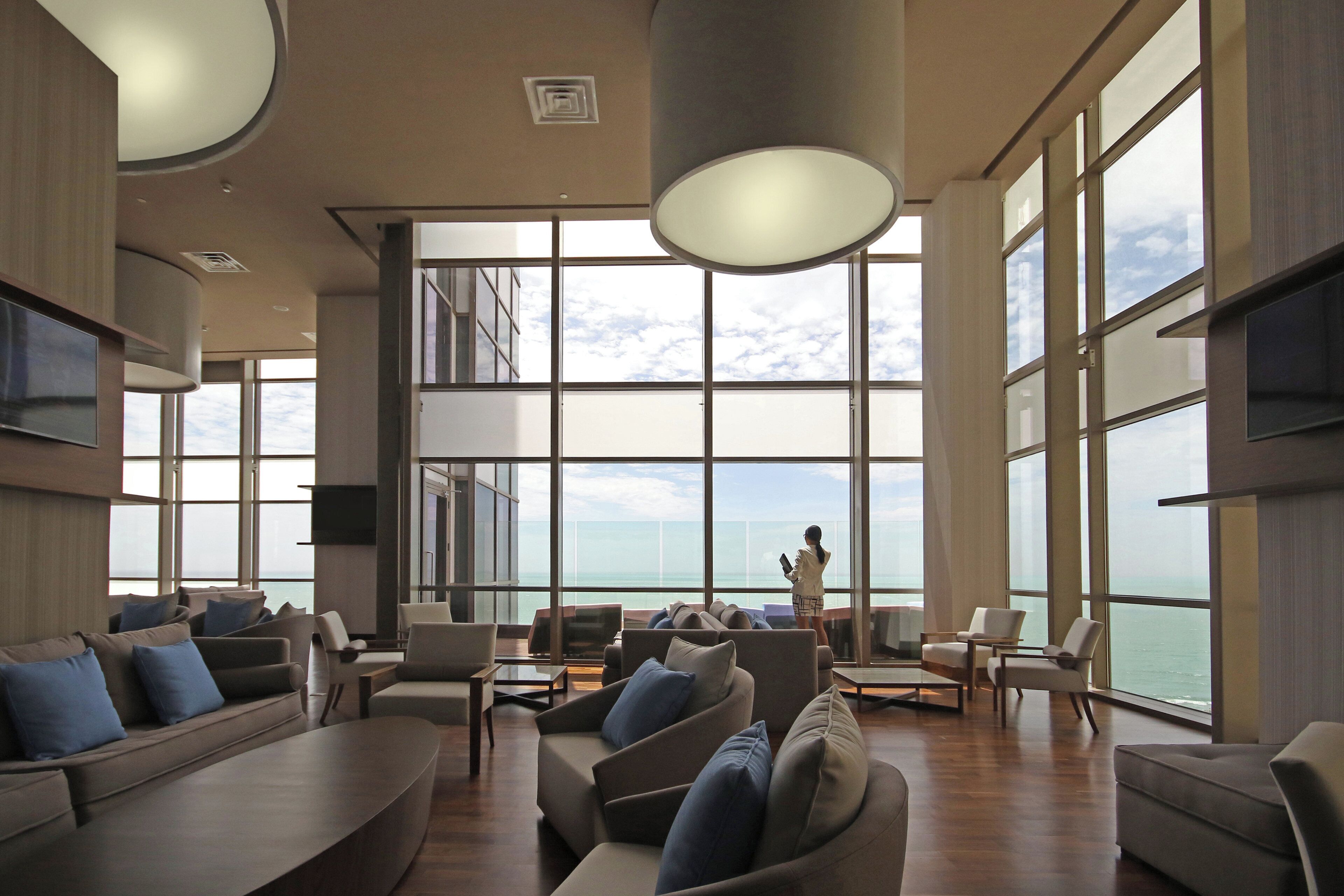 A spacious lounge with large windows, a high ceiling, and a view of the ocean.