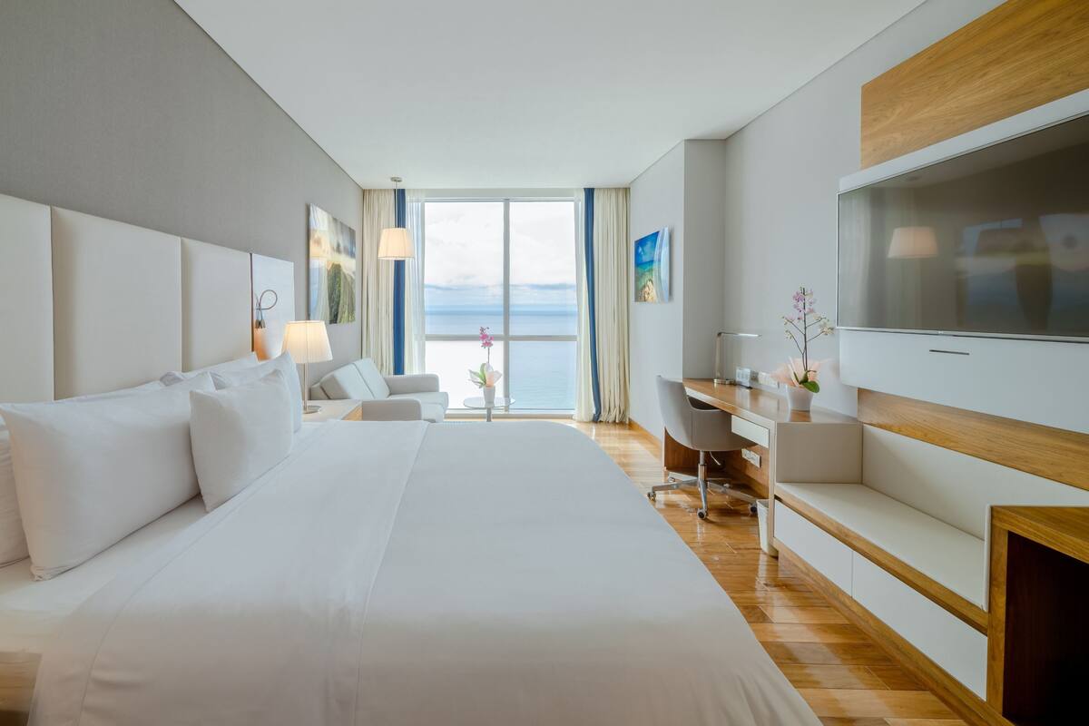 Een moderne hotelkamer met een groot bed, een bureau, een televisie en uitzicht op zee.