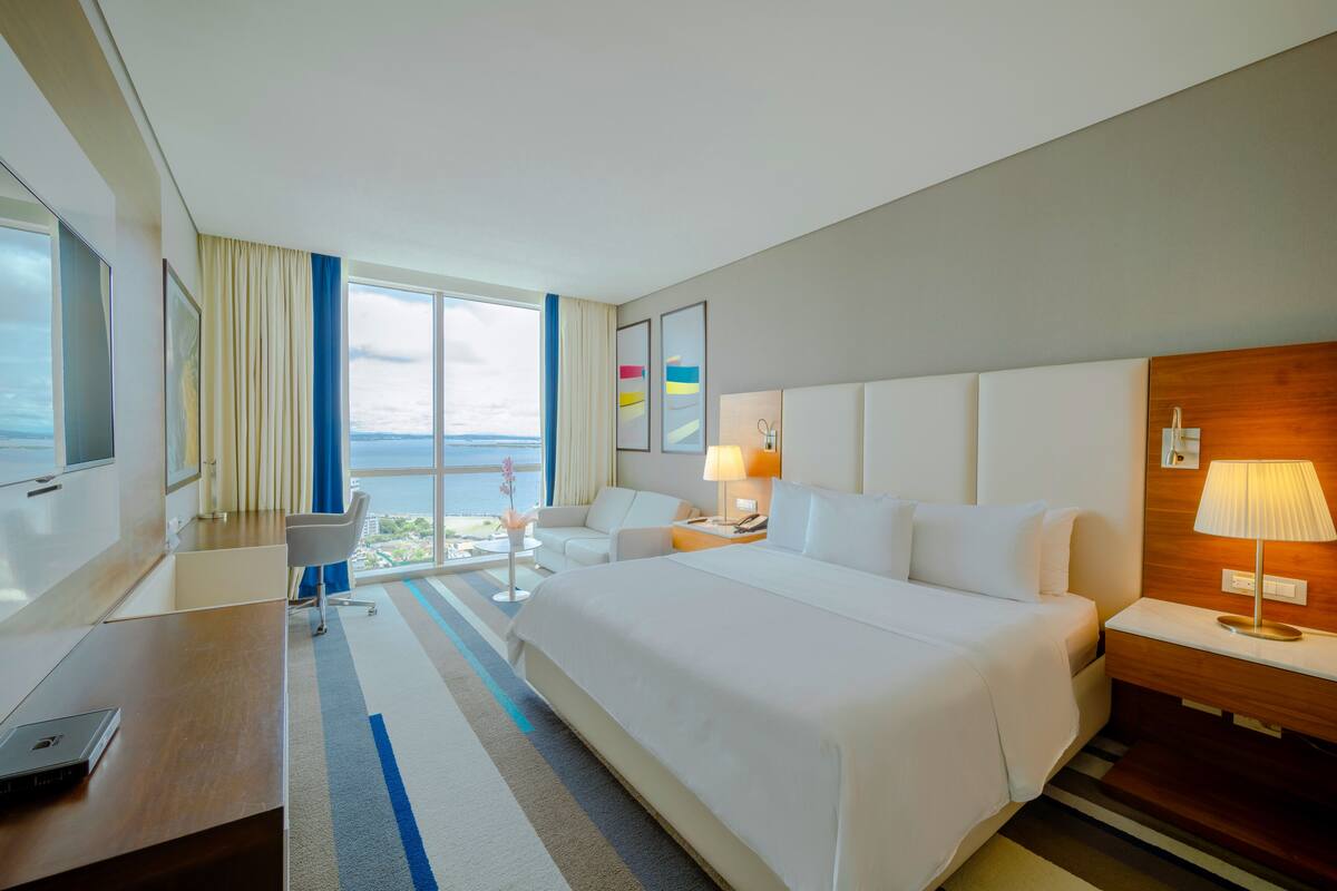 Een moderne hotelkamer met een groot bed, een bureau, een stoel en uitzicht op zee.