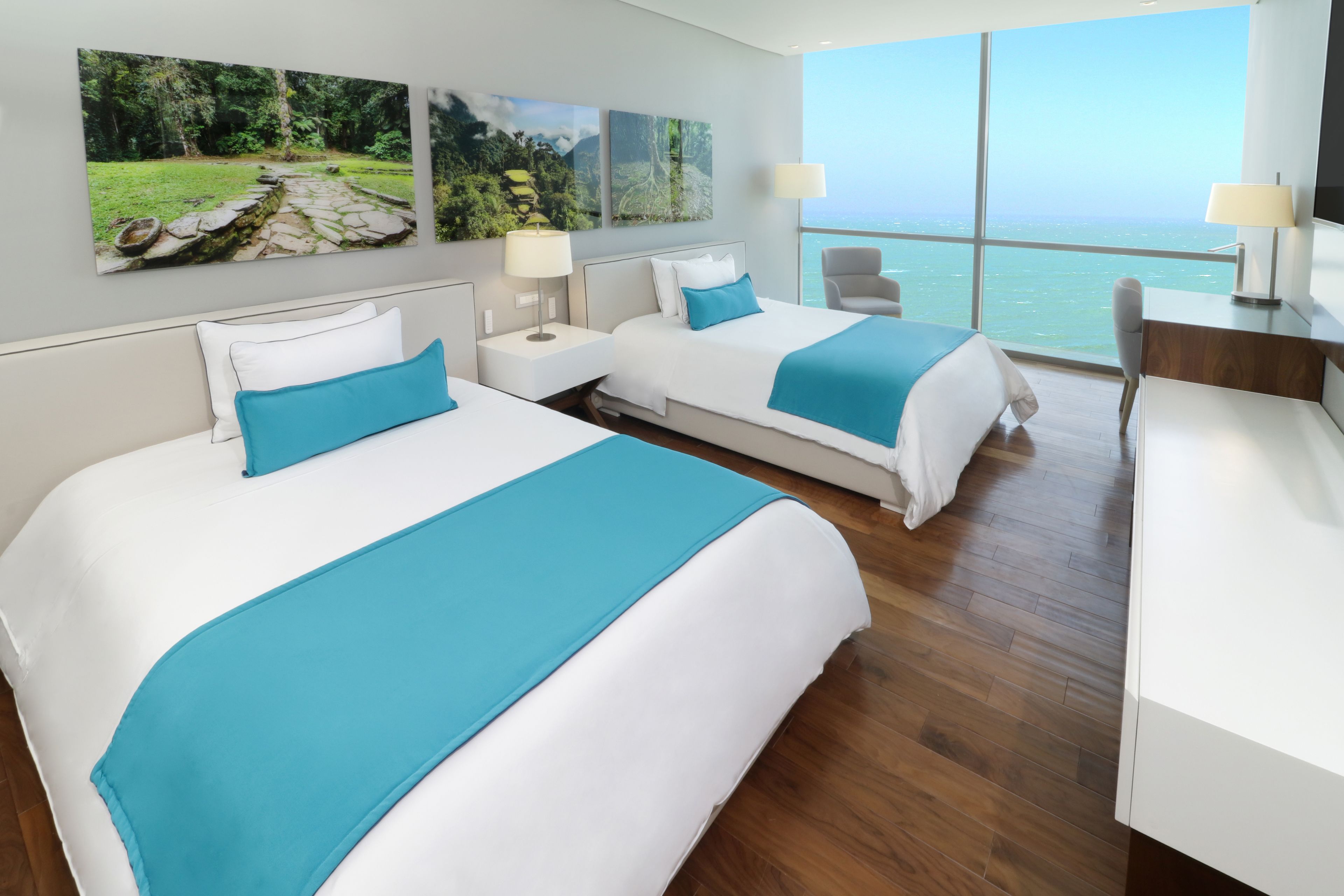 Habitación de hotel con dos camas, un escritorio, una silla y un ventanal con vista al mar.