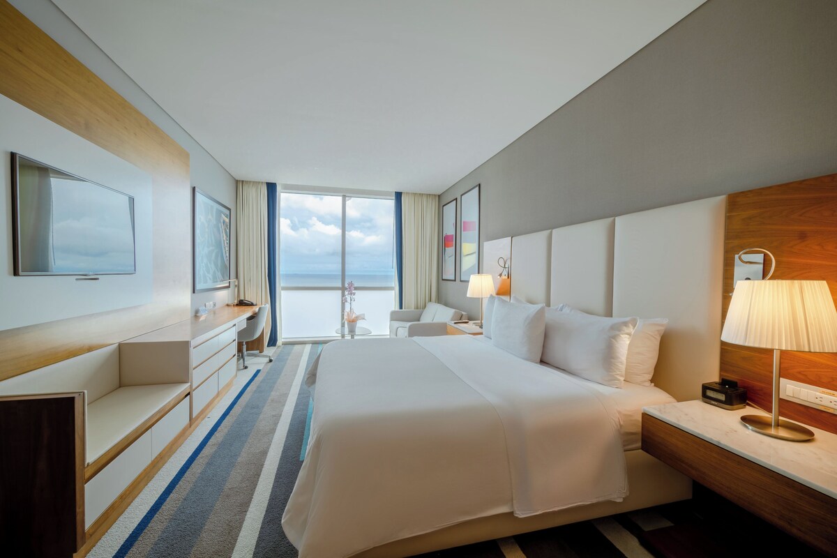 Habitación de hotel con una cama grande, un escritorio, una silla, un televisor y vista al mar.