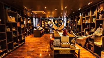 A boutique hotel lobby with wooden flooring, a central seating area, and shelves filled with bags and accessories.