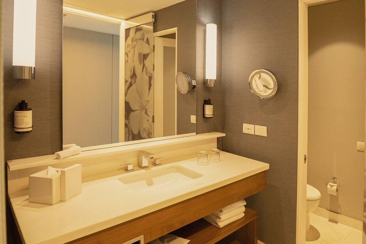 Een badkamer met een grote spiegel, een wastafel en een toilet. Handdoeken en toiletartikelen liggen op de wastafel.