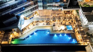 Vista aérea de un edificio moderno con un patio central que cuenta con una piscina, rodeado de diferentes zonas de estar y un pequeño escenario.
