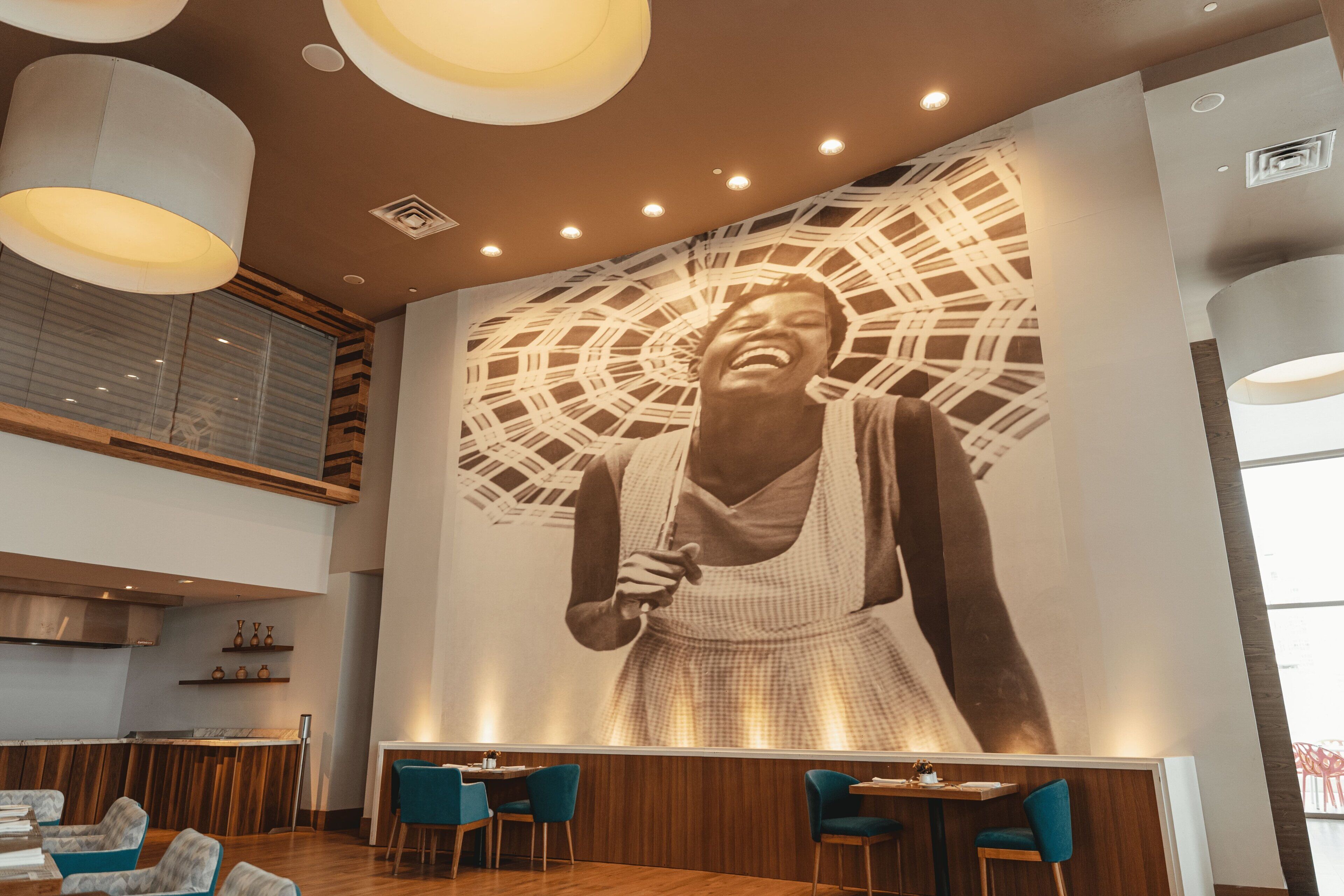 A restaurant with a large mural, wooden ceiling, and blue chairs.