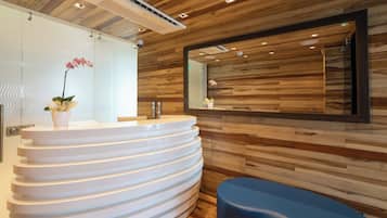 Un baño moderno con un mueble de tocador blanco y curvo, un panel de pared de madera, un espejo grande y un banco azul.