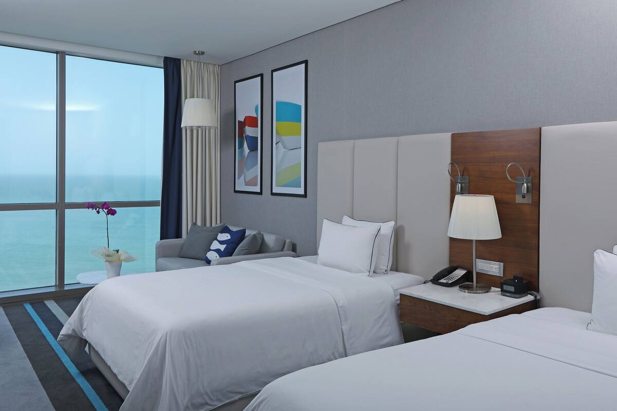 Een hotelkamer met twee bedden, een nachtkastje met een lamp, een telefoon en uitzicht op de oceaan.