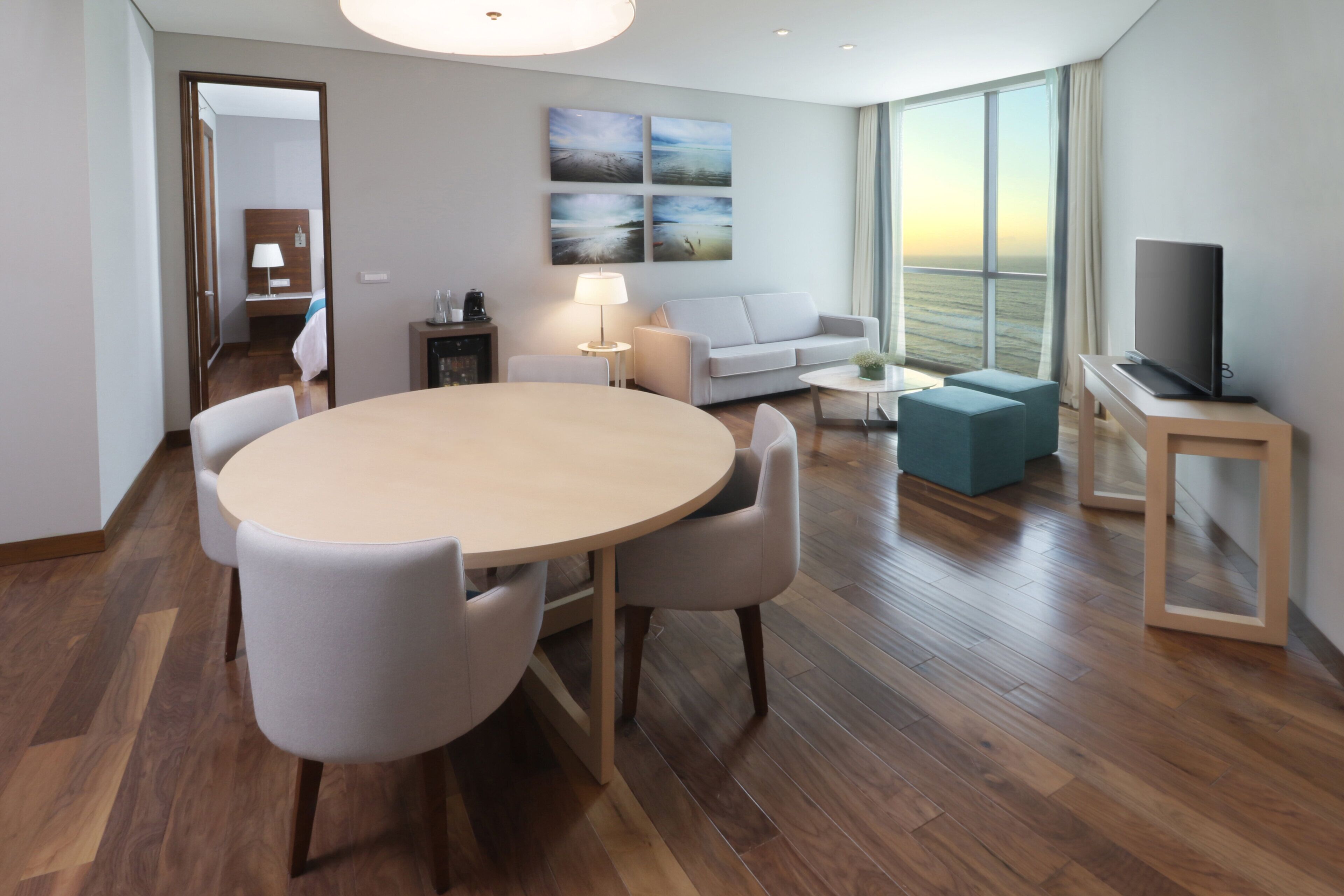 A modern living room with a round table, a sofa, a TV, and a large window with a view.