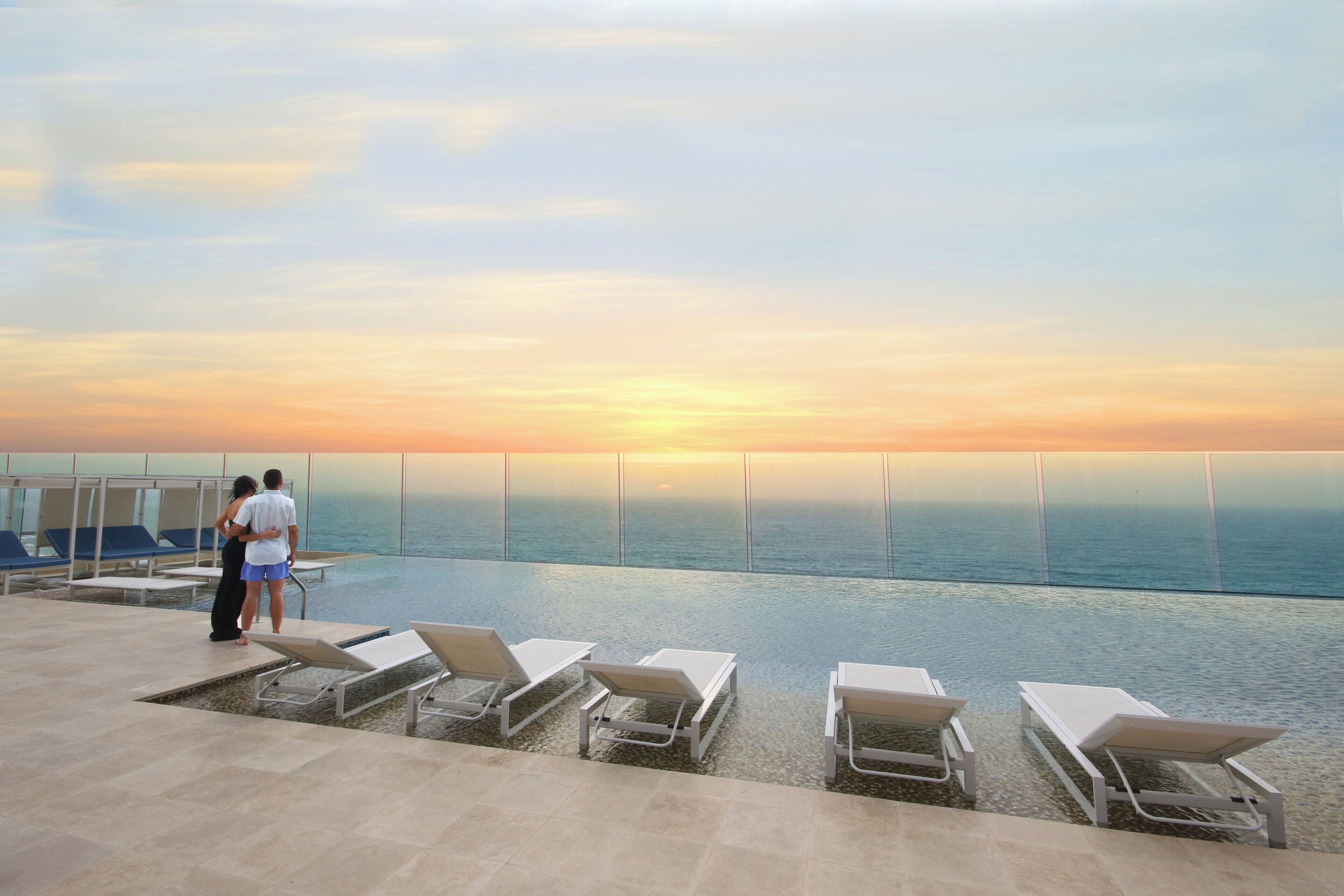 Zona de piscina con sillones de descanso y vista al océano al atardecer.