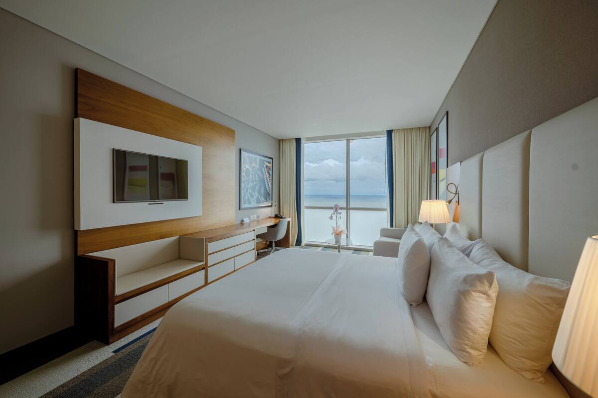 Een moderne hotelkamer met een groot bed, een bureau, een televisie en uitzicht op zee.