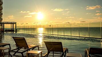 An infinity pool with lounge chairs, a view of the ocean, and a sunset.