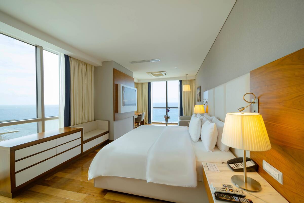 Hotelkamer met een groot bed, een bureau, een stoel, een televisie, een lamp en uitzicht op de oceaan.