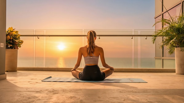 A person sitting on a yoga mat in a room with a view of the sunset over the ocean. - InterContinental Cartagena De Indias by IHG (Cartagena)