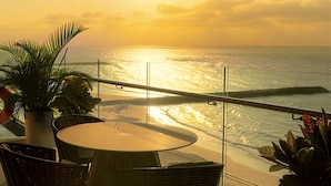 Un balcón con mesa y sillas frente a una playa al atardecer.