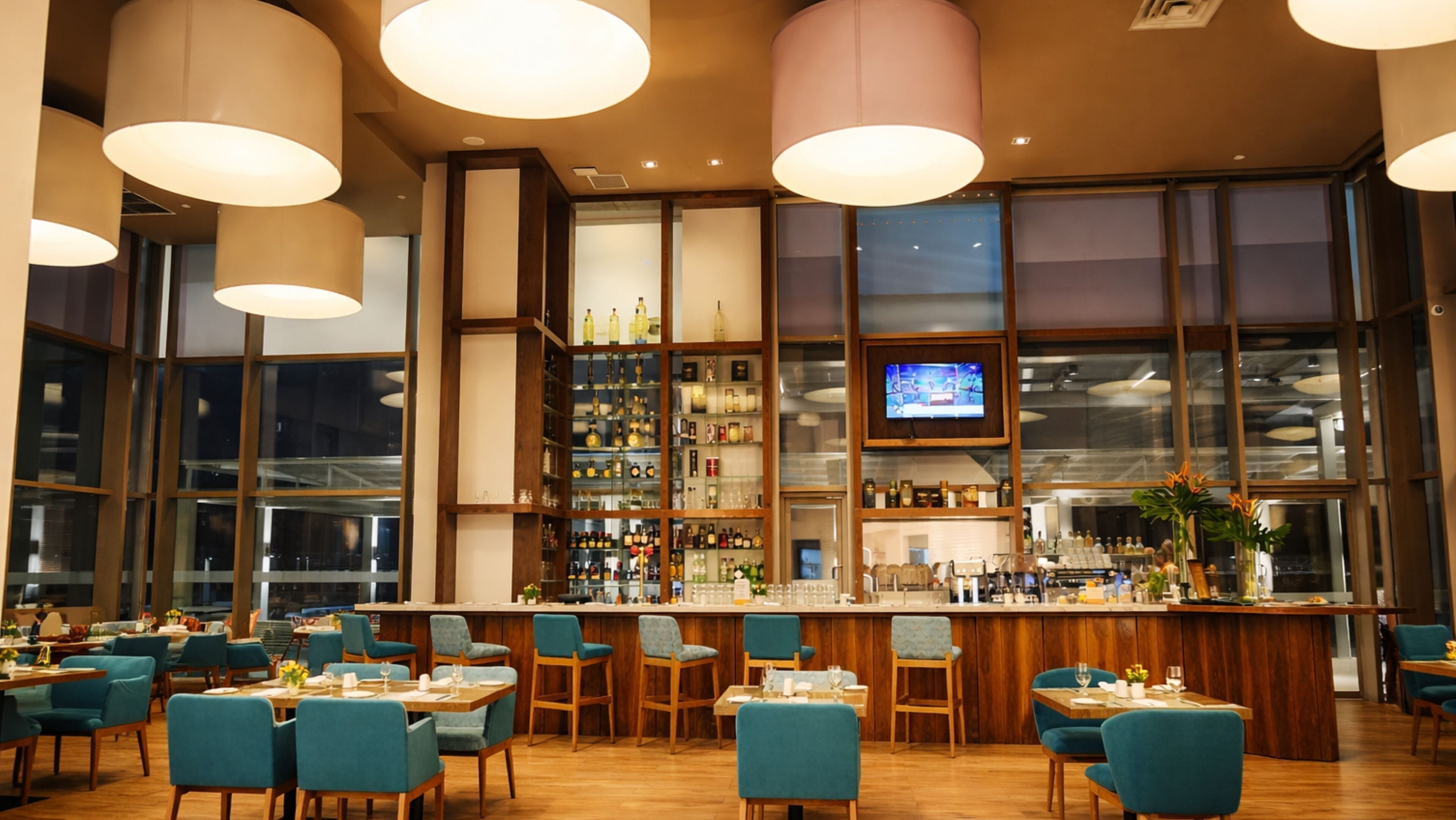 A restaurant with a bar area, wooden furniture, and large windows.