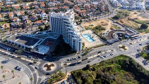 An aerial view of a hotel with a modern design, featuring a large building with multiple floors, a swimming pool, and a parking area. - Tamara Ashkelon (Ashkelon)