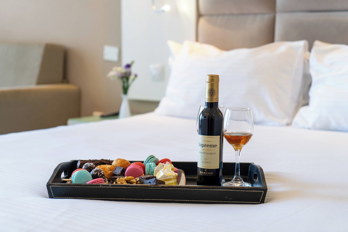 A bed with a tray of assorted pastries and a bottle of wine.