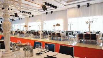 Un amplio salón de banquetes con varias mesas dispuestas para comer, elegantes candelabros y un diseño de techo moderno.