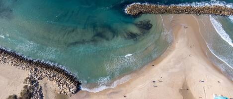 An aerial view of a beach with clear water, a rocky breakwater, and a few people.