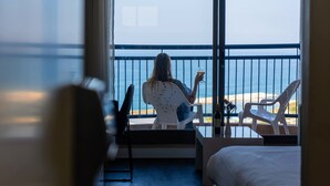 A room with a balcony overlooking a beach. There is a bed, a chair, and a table with a drink. - Tamara Ashkelon (Ashkelon)