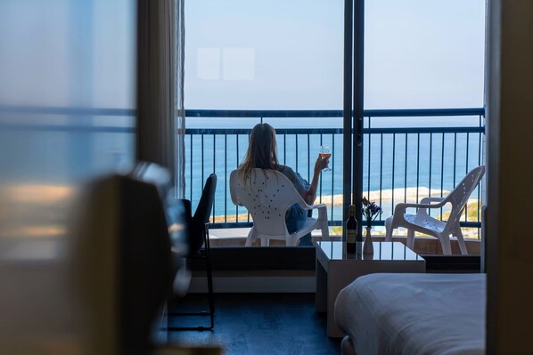 A room with a balcony overlooking a beach. There is a bed, a chair, and a table with a drink. - Tamara Ashkelon (Ashkelon)
