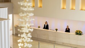 A hotel reception area with a modern design, featuring a reception desk, a decorative light fixture, and a staircase. - Tamara Ashkelon (Ashkelon)