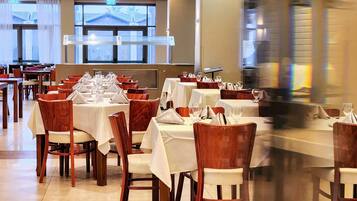 Una sala ristorante con diversi tavoli apparecchiati, sedie in legno e tovaglie bianche.