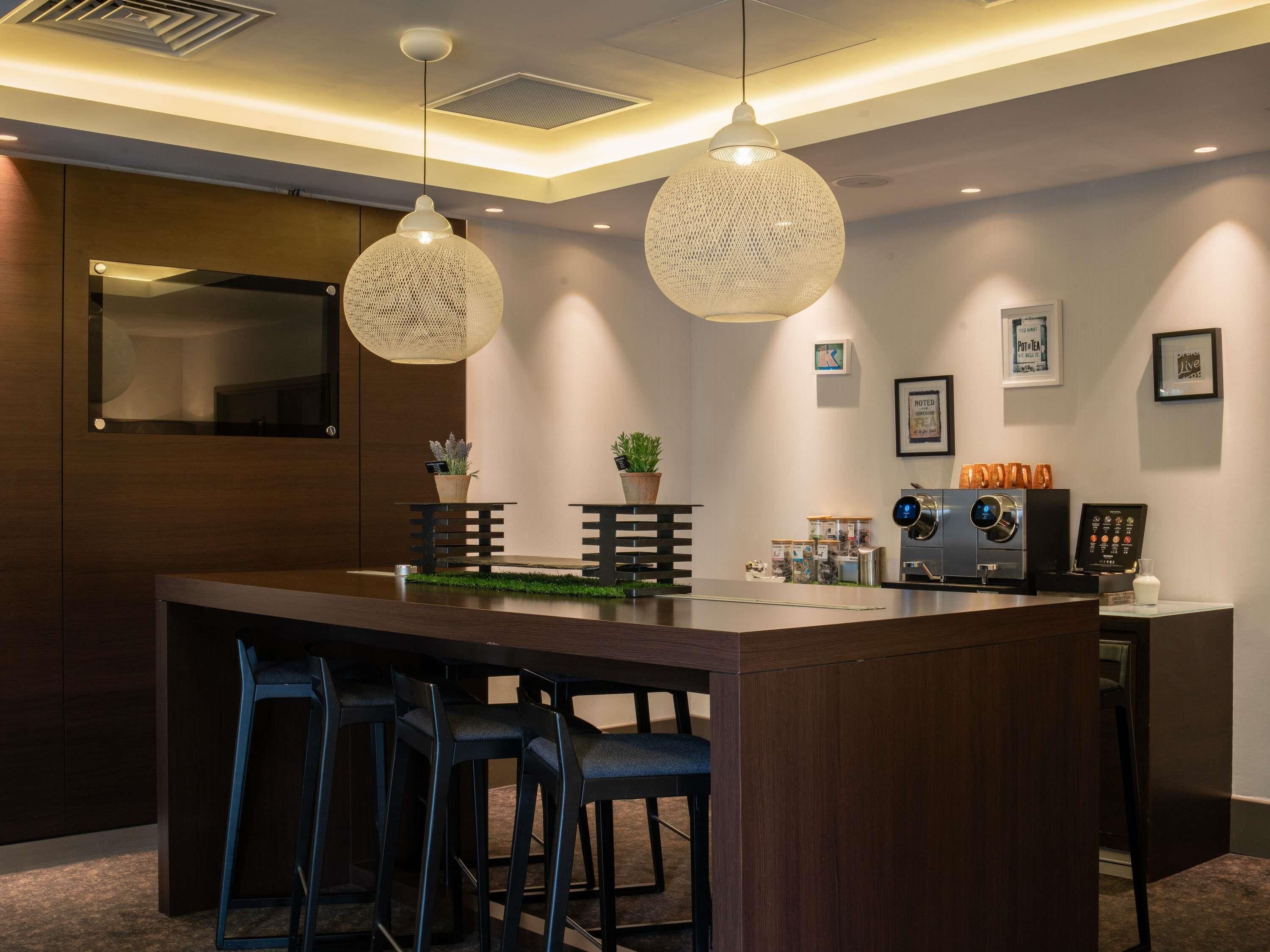 Een moderne bar met een houten toonbank, twee hangende pendelverlichting en een koffieapparaat.