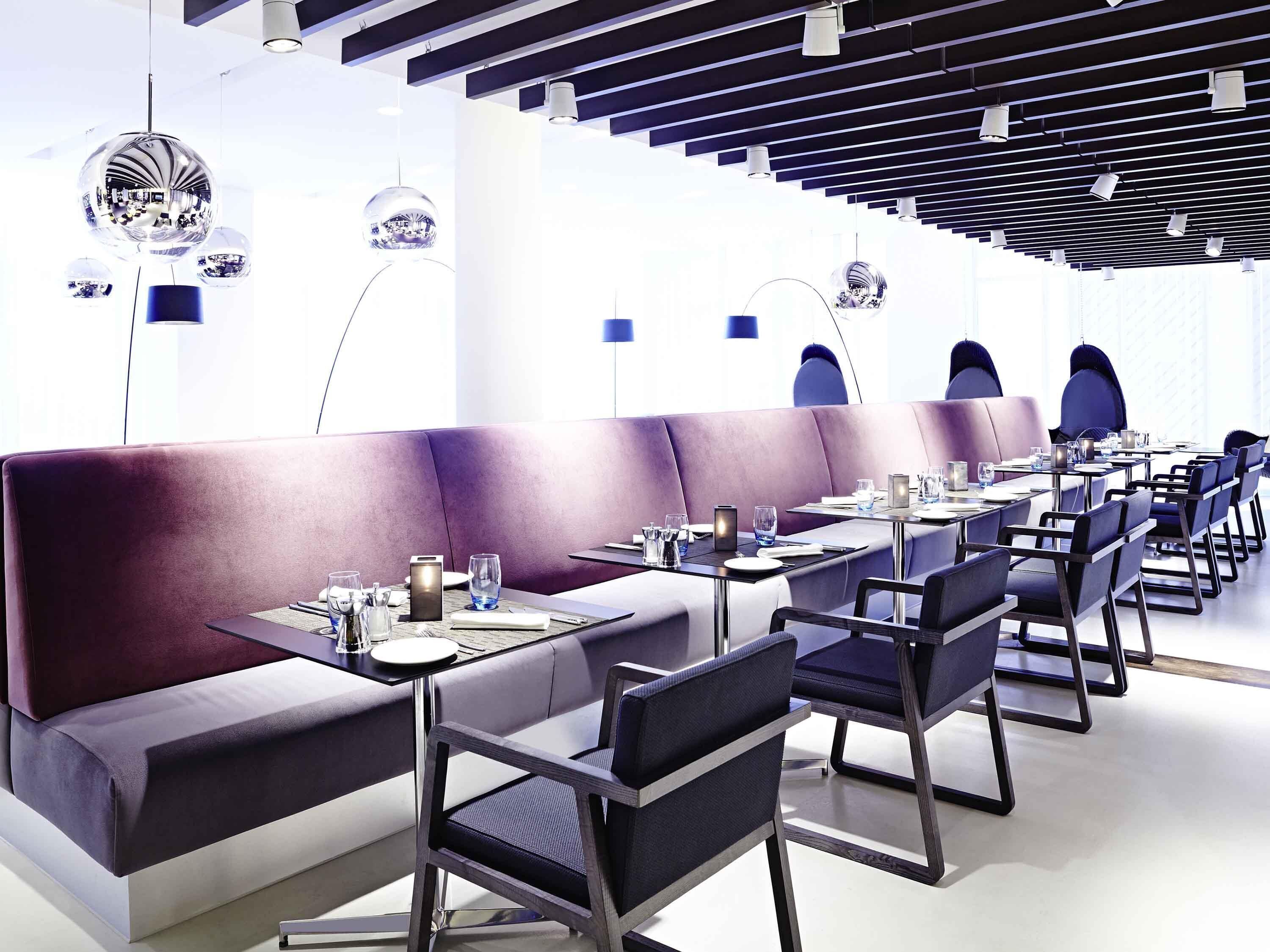 Un restaurant moderne doté d’un long comptoir, de banquettes violettes et de luminaires suspendus sphériques originaux.