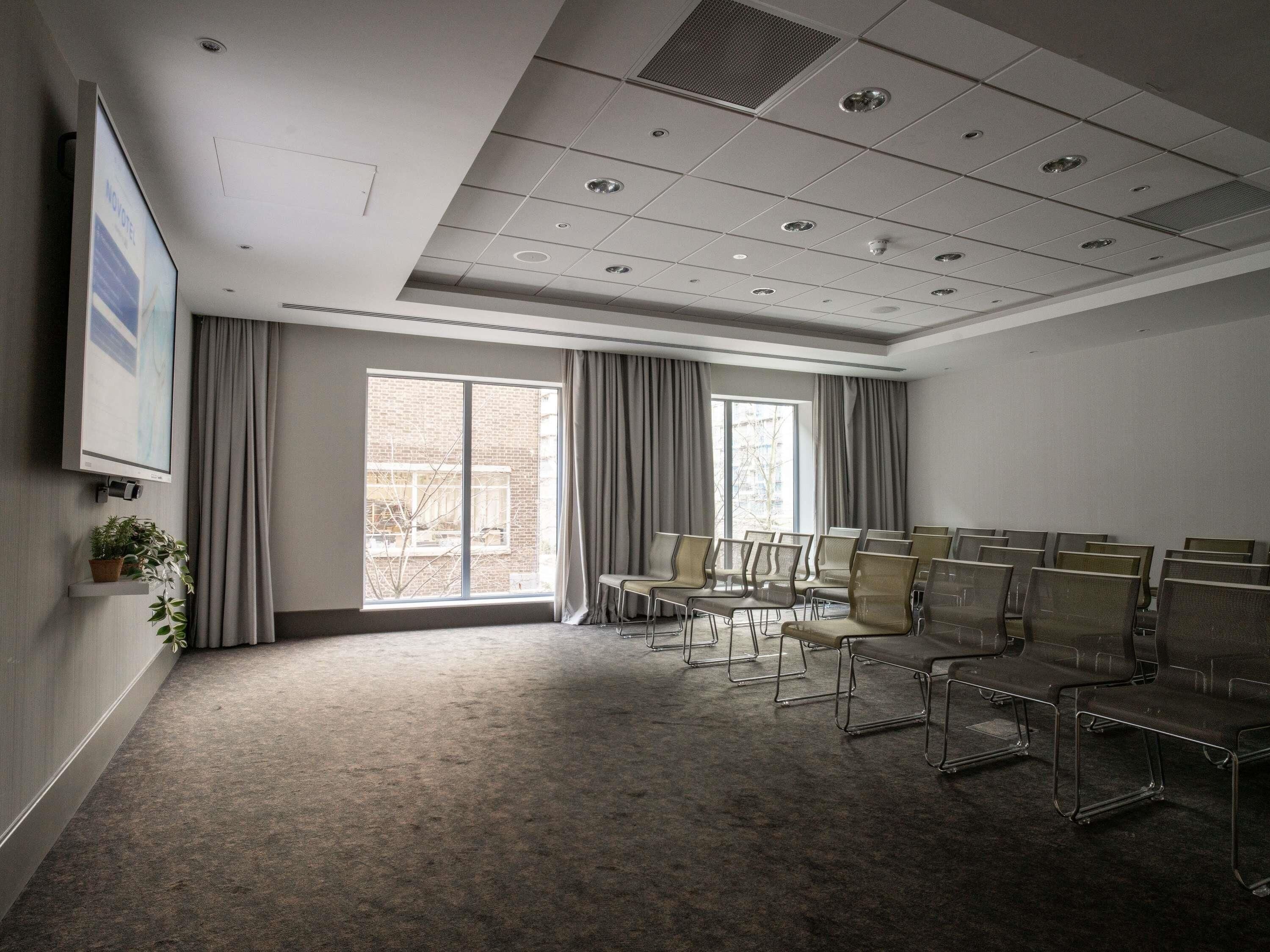 A conference room with a large window, a projector screen, and rows of chairs.