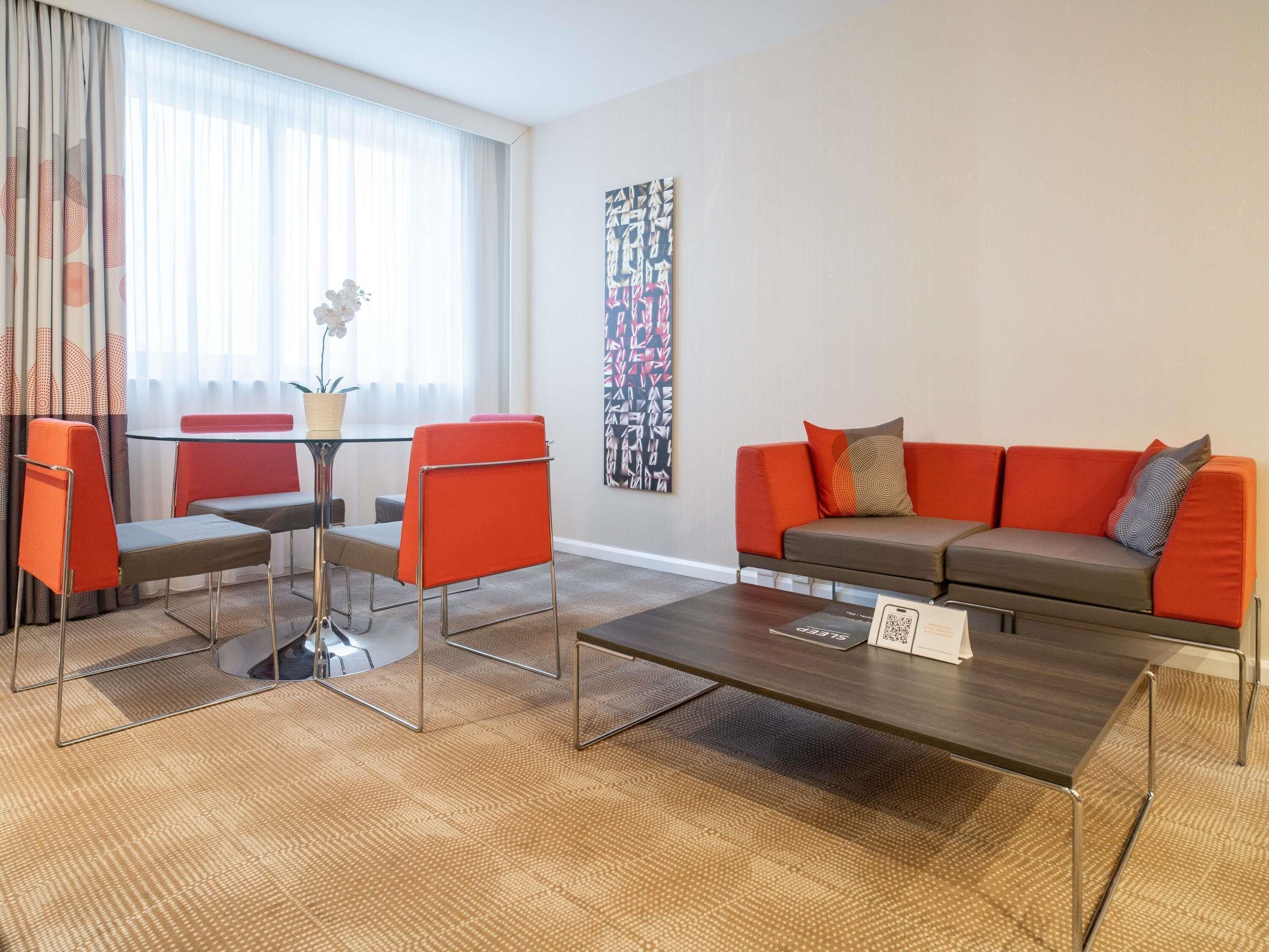 A modern living room with a sofa, chairs, a coffee table, and a large abstract painting on the wall.
