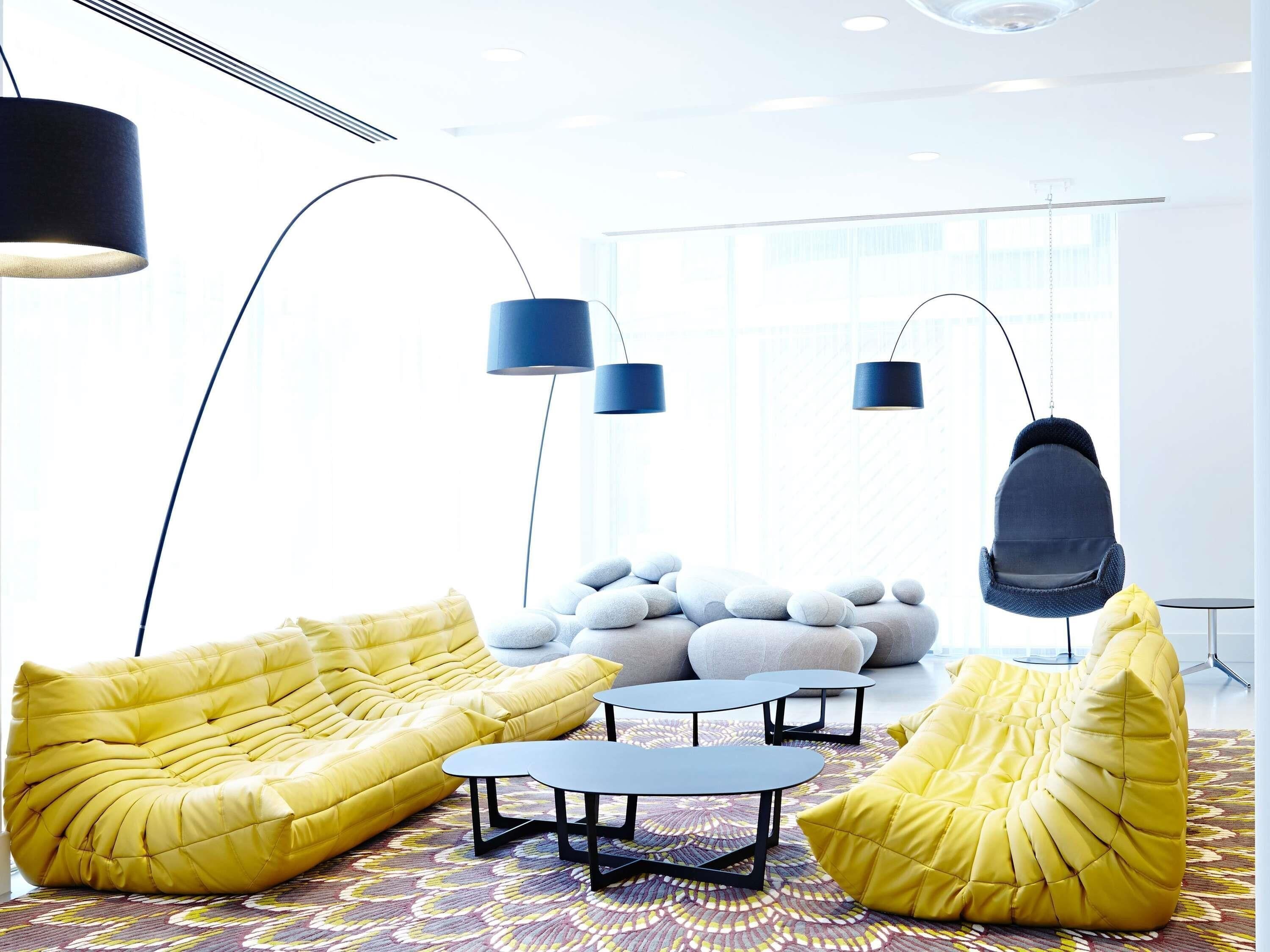 Un salon moderne avec des fauteuils en forme de poire de couleur jaune, une table basse ronde et un fauteuil suspendu.