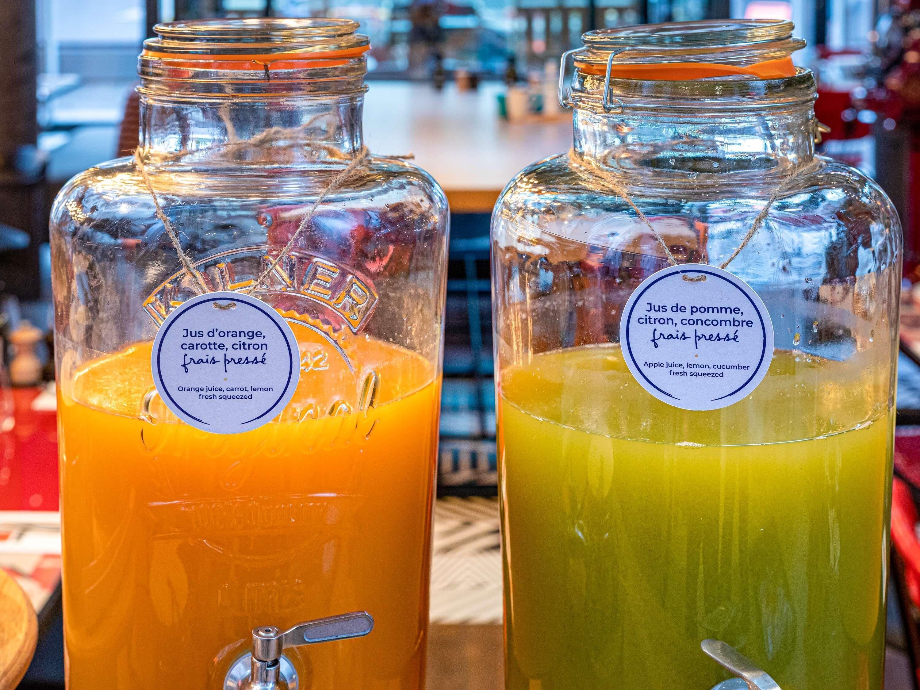 Deux bouteilles en verre, toutes deux munies d’une étiquette, l’une contenant du jus d’orange et l’autre un mélange de jus verts.
