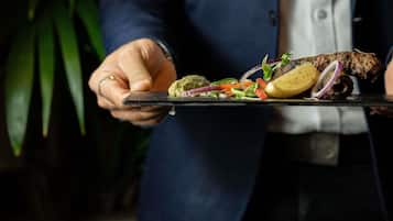 Una persona sosteniendo un plato con comida, incluyendo un trozo de carne, verduras y una rebanada de pan.