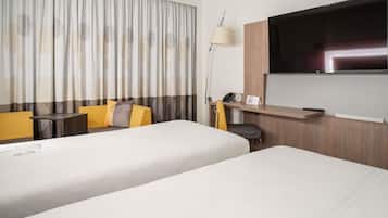 Une chambre d’hôtel avec deux lits, un bureau, une chaise, une télévision et une lampe.