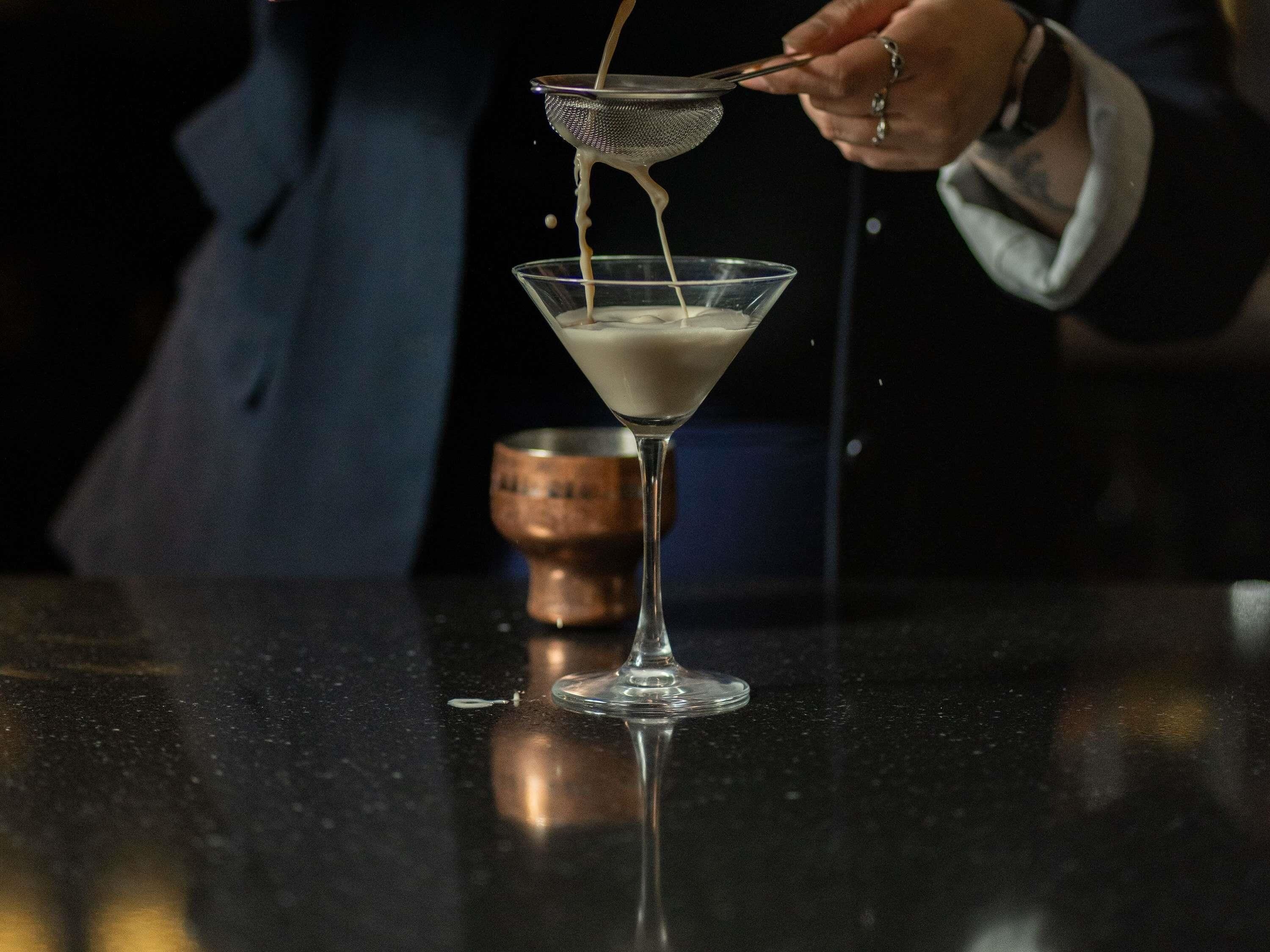 A person pouring a liquid into a martini glass.