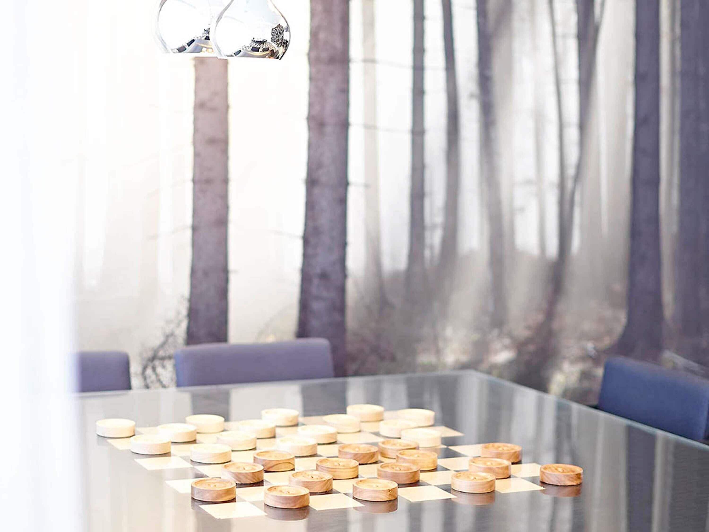 A modern dining table with a glass top, surrounded by wooden chairs, set in a room with a forest view.