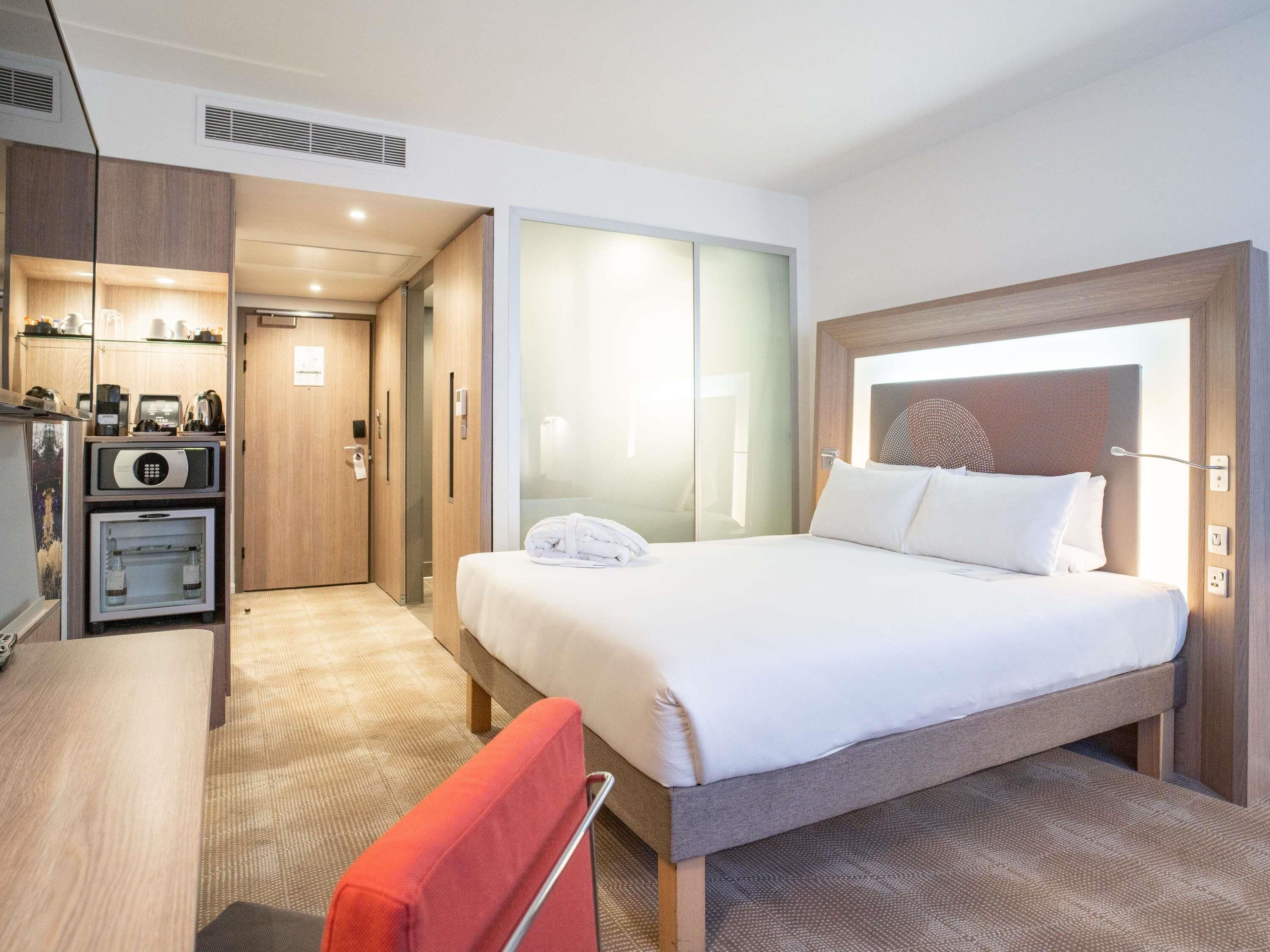 Una habitación de hotel con cama, escritorio, silla, minibar y baño.