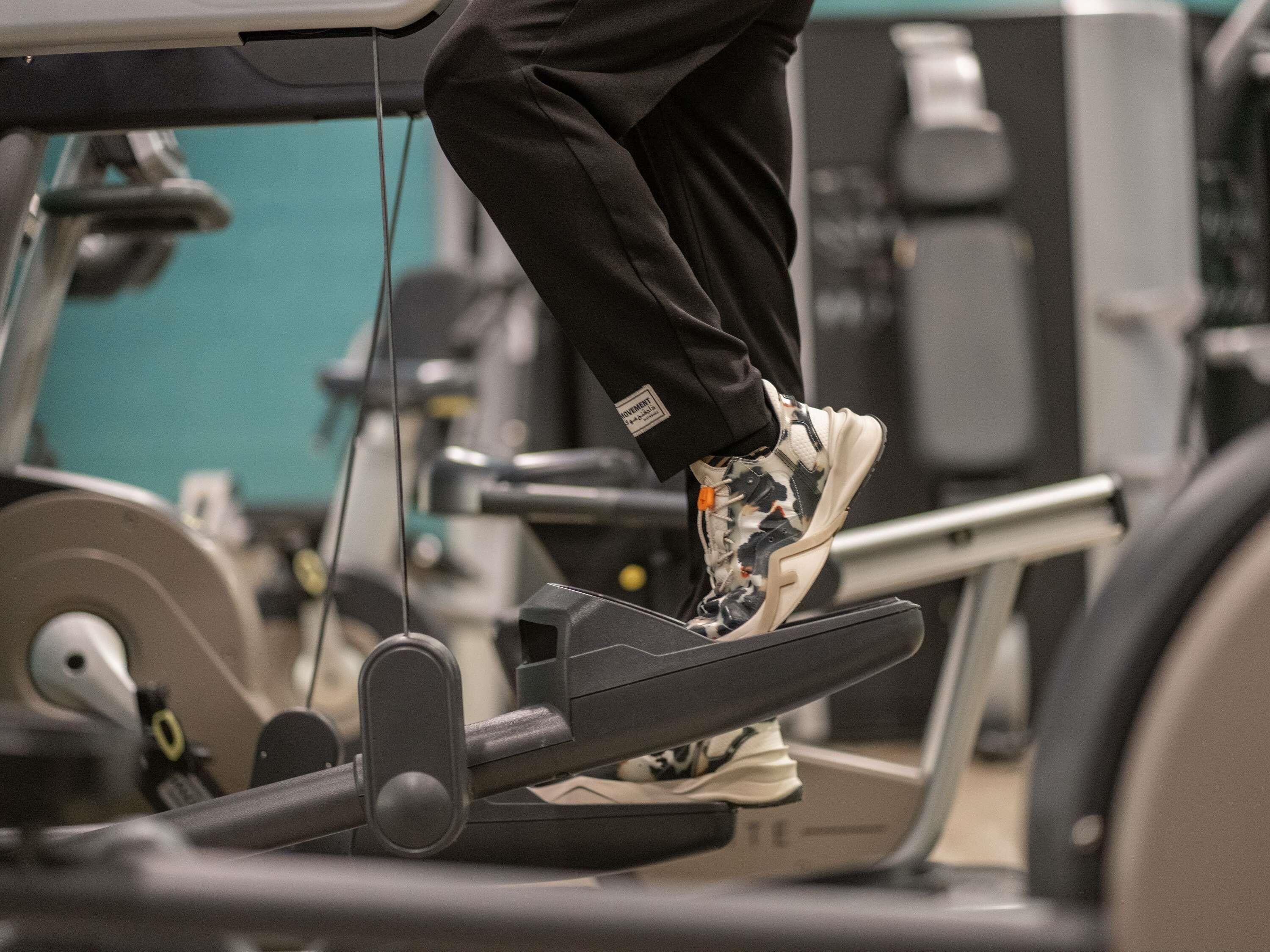 A treadmill with a person using it, a weight stack, and a cable machine in the background.