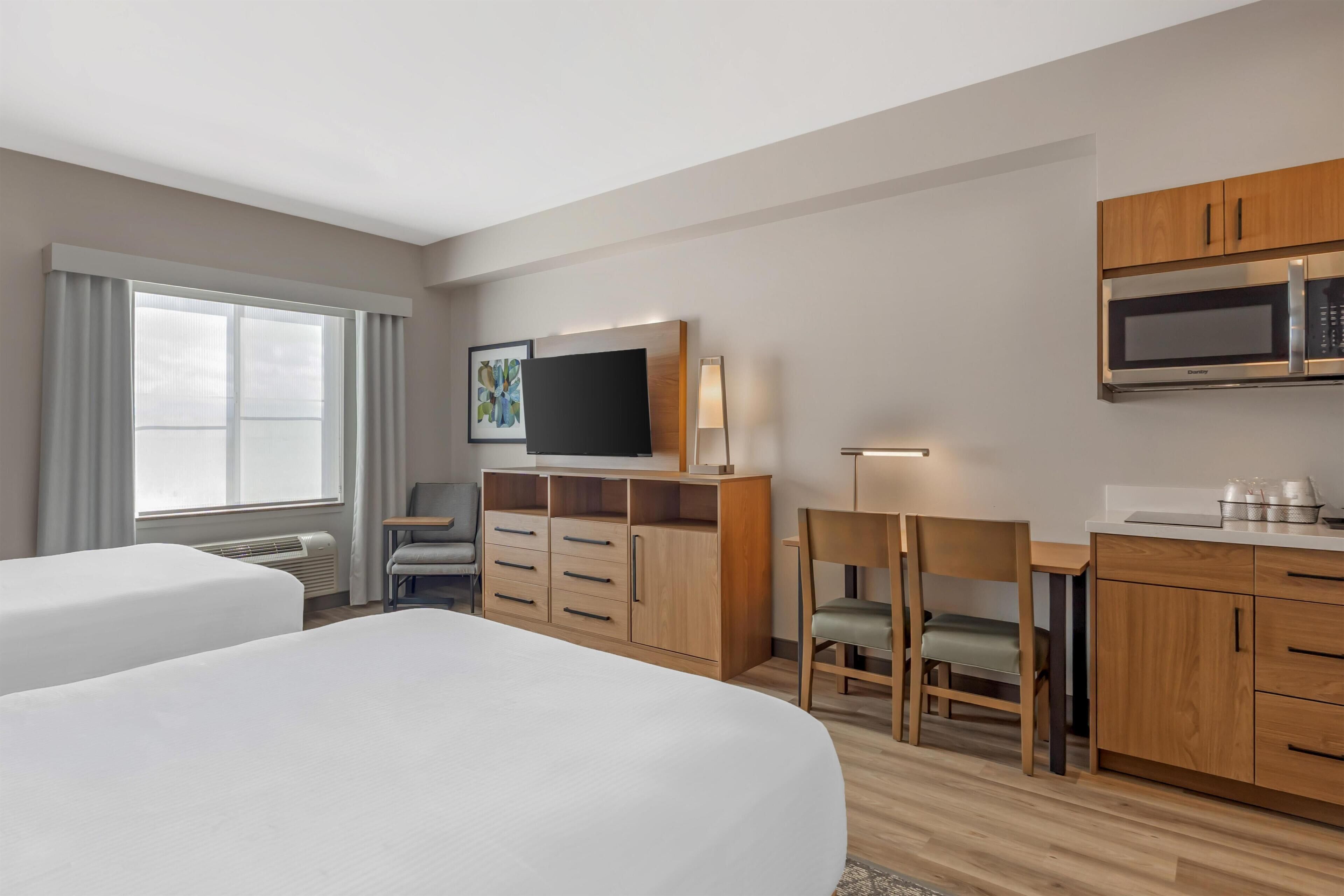 A hotel room with two beds, a desk, a chair, a television, a microwave, and a cabinet.
