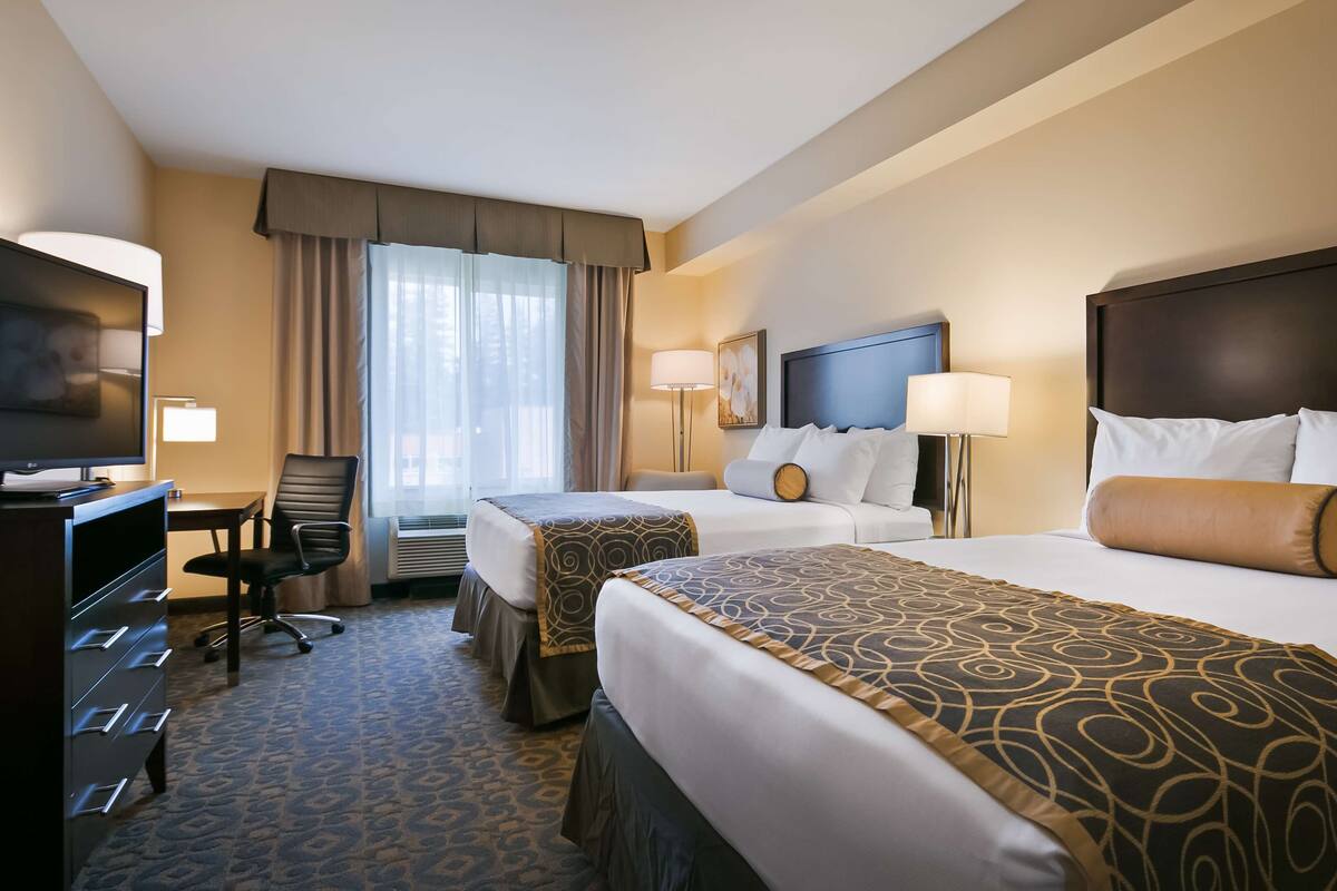 A hotel room with two beds, a desk with a television, and a chair.
