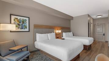 A hotel room with two beds, a desk, a chair, a lamp, and a painting on the wall.