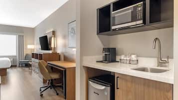 Une chambre d’hôtel équipée d’un lit, d’un bureau, d’une chaise et d’une kitchenette comprenant un four à micro-ondes, une machine à café et un lave-vaisselle.