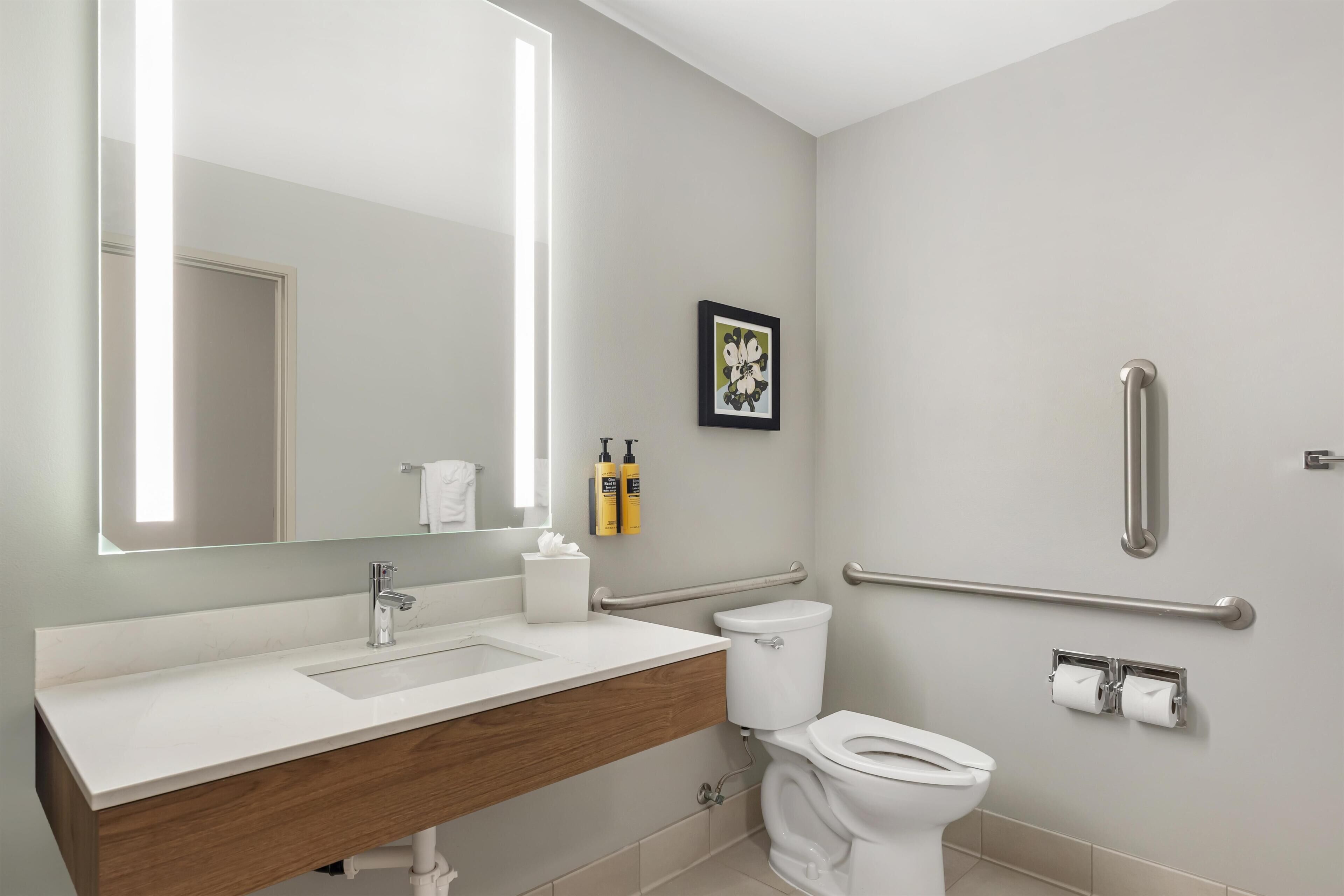 Een moderne badkamer met een grote spiegel, een wastafel, een toilet en handgrepen.