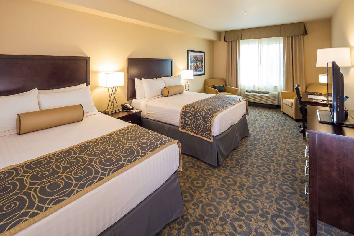 A hotel room with two beds, a desk with a computer, a chair, and a window with curtains.