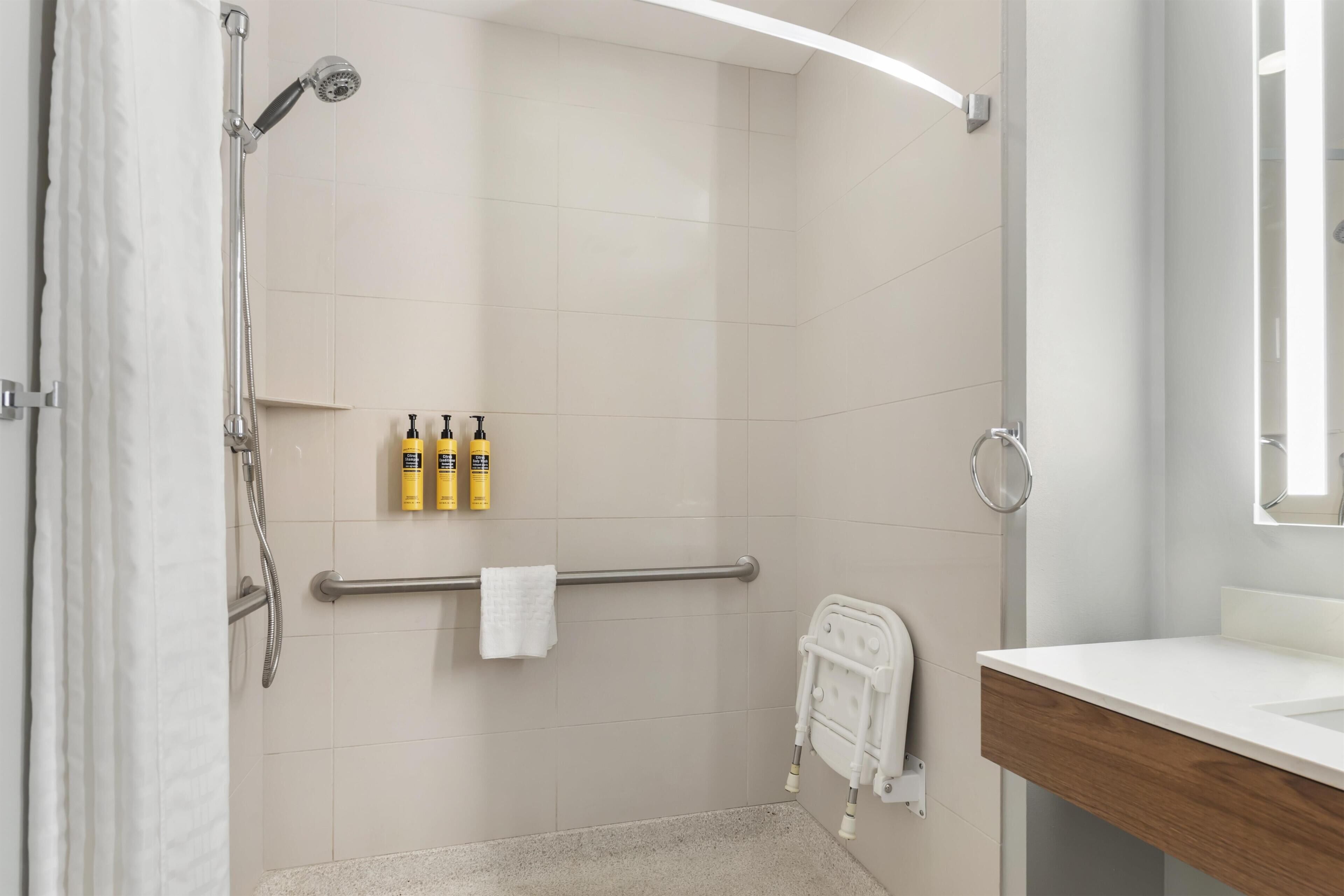 A modern bathroom with a shower, a handrail, and three bottles of shampoo.