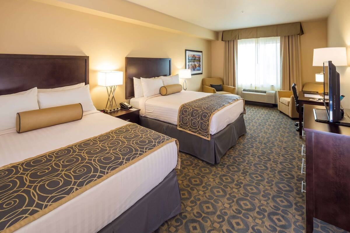 A hotel room with two beds, a desk, a chair, a TV, and a window with curtains.