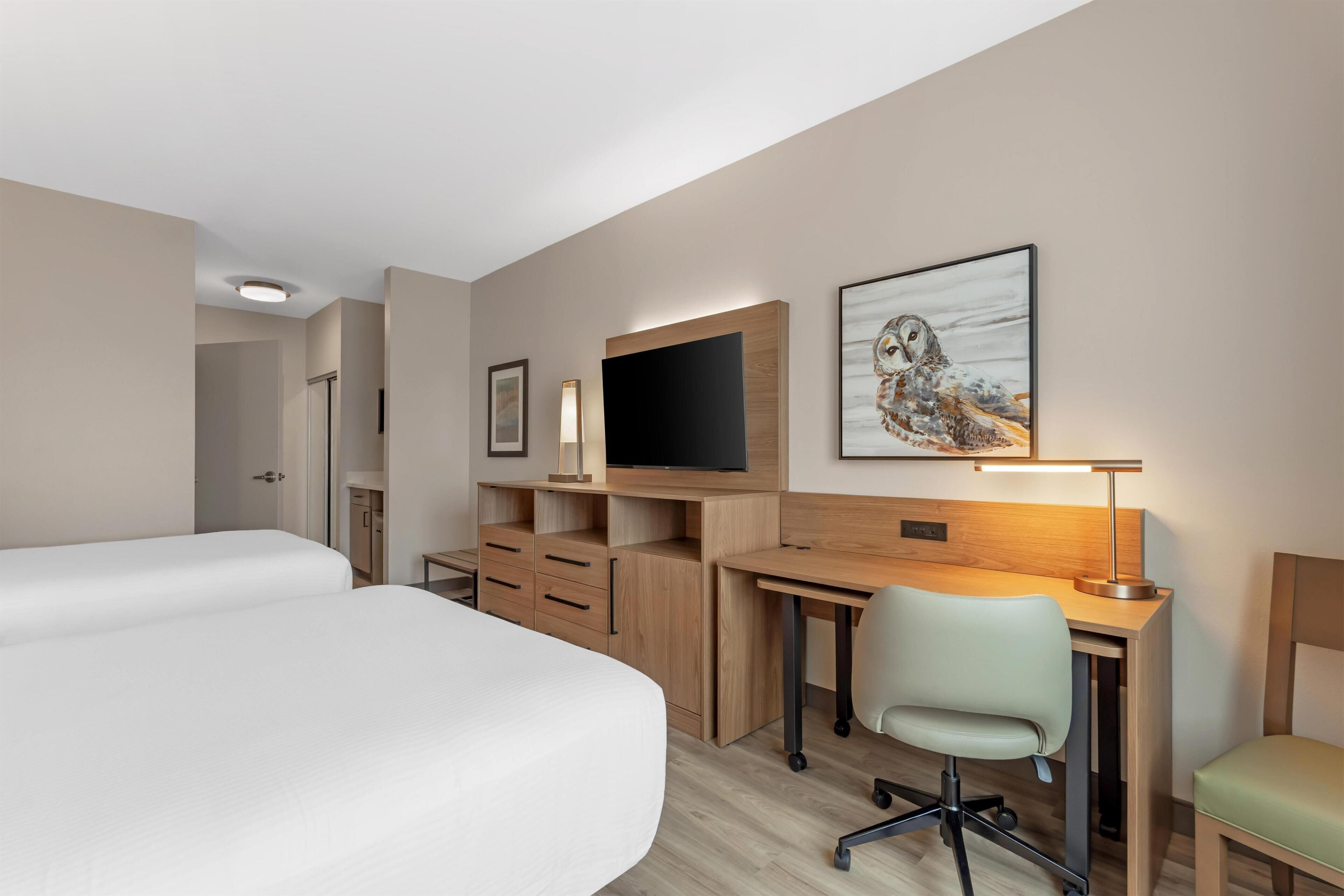 A hotel room with a bed, a desk, a chair, a television, and artwork on the wall.